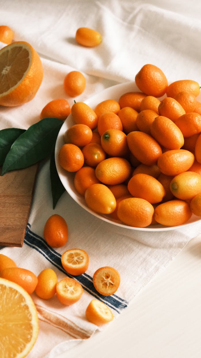 Bowl of bright kumquats with orange slices on elegant white cloth setup.