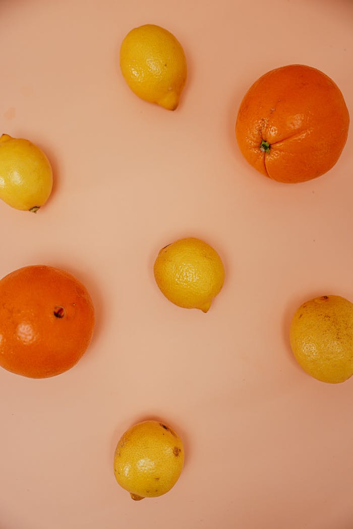 A vibrant arrangement of citrus fruits including oranges and lemons on a pink surface.