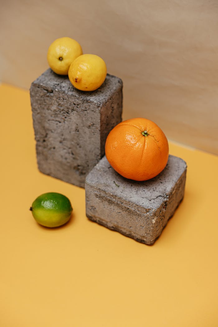 Artistic arrangement of citrus fruits on concrete blocks with vibrant background.